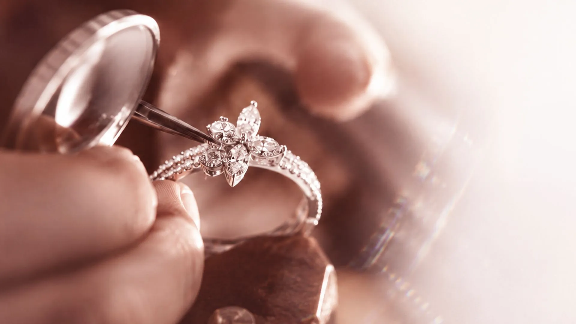 A jeweller setting marquise diamonds into a floral white-gold ring with tweezers under a loupe